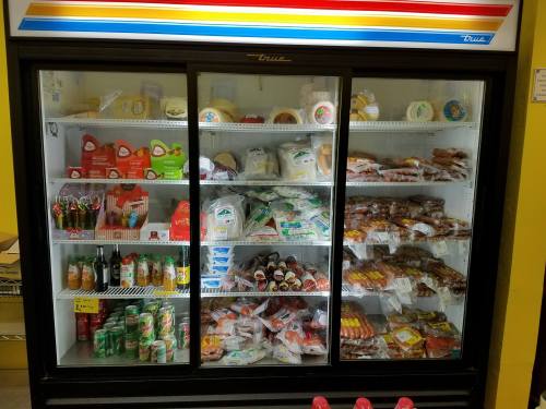 A glass-front refrigerator filled with various packaged foods, drinks, and frozen items.