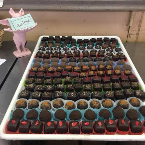 A tray filled with assorted chocolate confections, decorated with colorful toppings and a pink pig figurine holding a sign.
