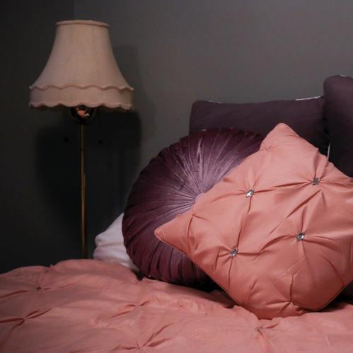 Cozy bedroom scene featuring decorative pillows on a bed and a vintage lamp with a scalloped shade.
