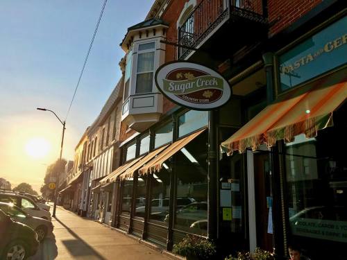 A charming storefront of Sugar Creek Country Store at sunset, with awnings and nearby parked cars.
