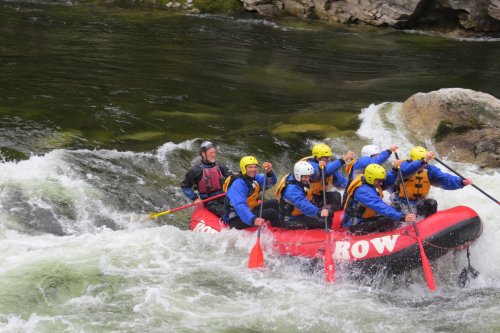 A group of people in a red raft navigating whitewater rapids, wearing helmets and life jackets.