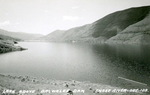 Black and white photo of a serene lake above Brownlee Dam, surrounded by mountains and reflecting the sky.