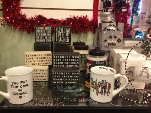 Display of teacher-themed mugs and signs with inspirational quotes about teaching and education, decorated for Christmas.