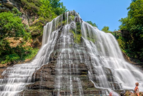 A majestic waterfall cascading down rocky cliffs, surrounded by lush greenery under a clear blue sky.