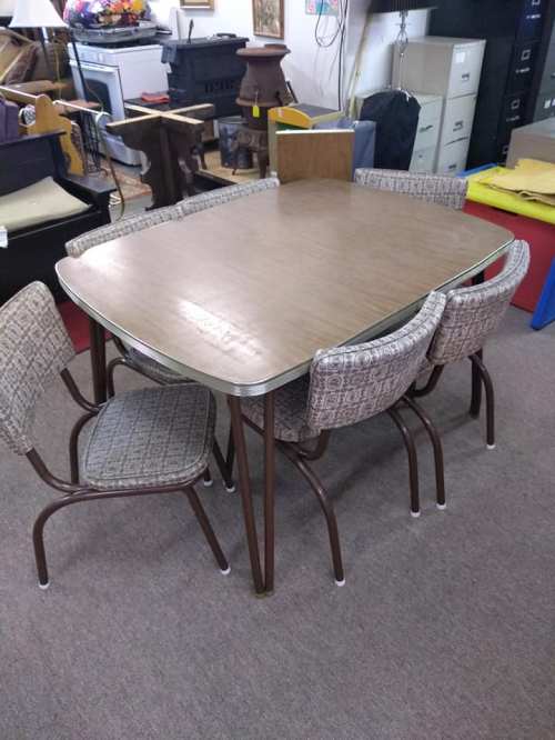 A square wooden dining table with four patterned chairs in a cozy indoor setting.