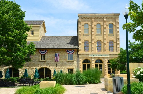 Historic stone building with large windows, greenery, and American flags, set against a clear blue sky.