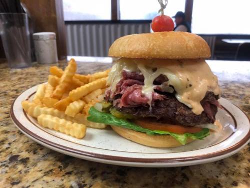 A hearty burger with roast beef, creamy sauce, lettuce, and tomato, served with crinkle-cut fries on a plate.