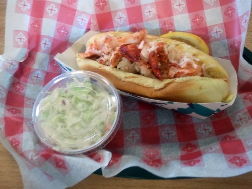 A lobster roll topped with lobster meat and coleslaw, served in a paper-lined tray.