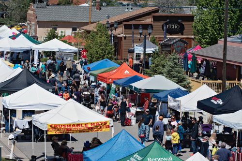 A bustling outdoor market with colorful tents and crowds of people enjoying the event on a sunny day.