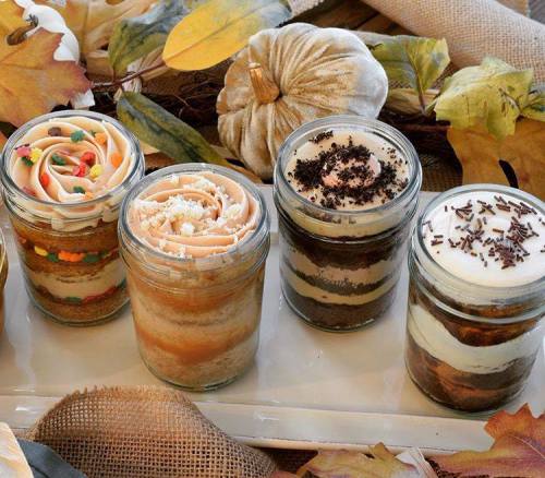 Four layered dessert jars with various toppings, surrounded by autumn leaves and decorative pumpkins.