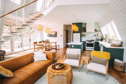 Bright, modern living space with a leather sofa, wooden dining table, and open kitchen featuring large windows and stylish decor.