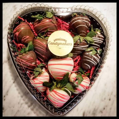 A heart-shaped box filled with chocolate-covered strawberries, decorated with drizzles and green leaves.