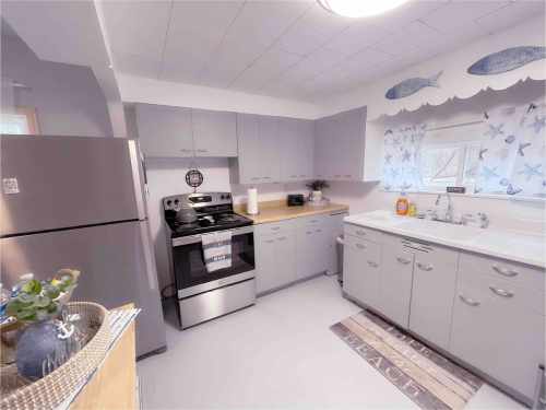 A modern kitchen with gray cabinets, stainless steel appliances, and a window adorned with a fish-themed curtain.