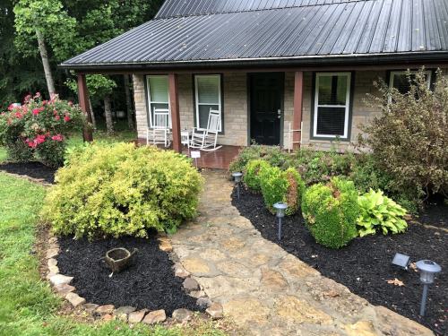 A stone pathway leads to a house with a black roof, surrounded by lush greenery and colorful flowers.