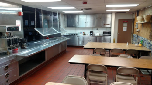 A clean kitchen with stainless steel appliances and several tables set up for dining.