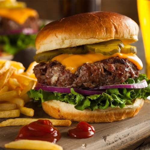 A juicy cheeseburger with lettuce, pickles, and onion, served with fries and ketchup on a wooden platter.