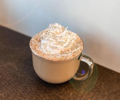 A clear glass mug filled with creamy coffee topped with whipped cream and a sprinkle of cocoa powder.