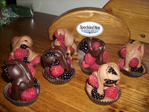 A display of chocolate-covered raspberries arranged in cups, with a sign for Speckled Hen Chocolate Co. in the background.