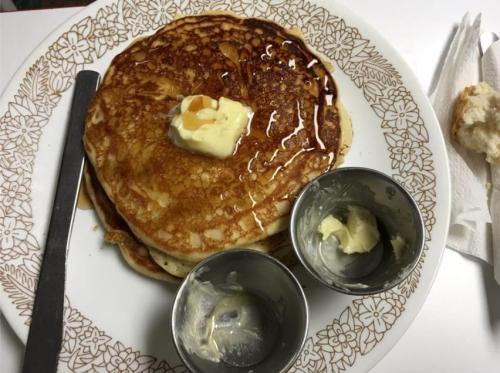 A plate of golden pancakes topped with butter and syrup, accompanied by two small containers of butter.