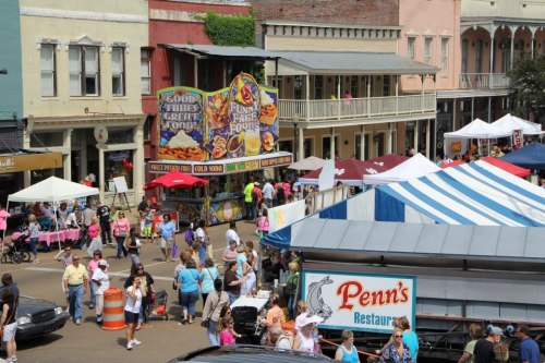 A bustling street fair with food stalls, colorful tents, and crowds of people enjoying the festivities.