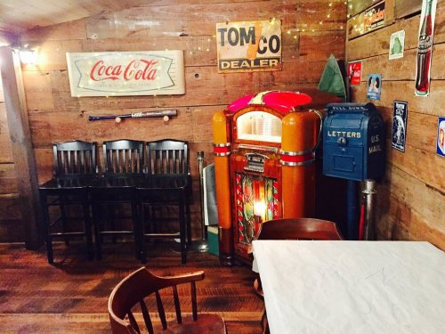 A cozy room with wooden walls, featuring a vintage jukebox, bar stools, and retro signs.