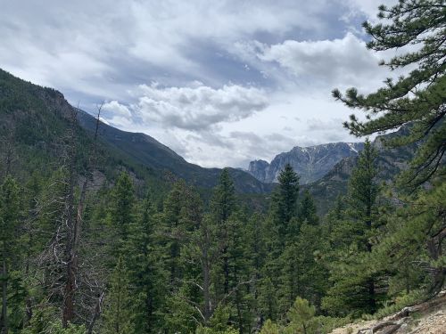 A scenic view of mountains and lush green trees under a cloudy sky.