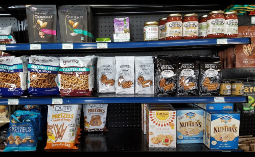 A shelf displaying various brands of pretzels, snacks, and jars of dip in a grocery store.