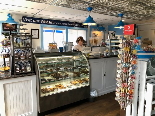 A cozy dessert shop with a glass display case of treats, colorful lollipops, and a barista behind the counter.