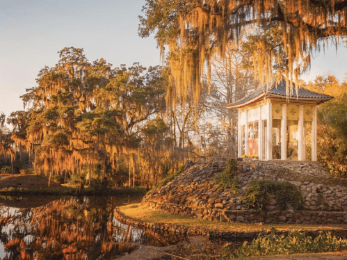 A serene gazebo by a pond, surrounded by trees draped in Spanish moss, illuminated by warm sunset light.