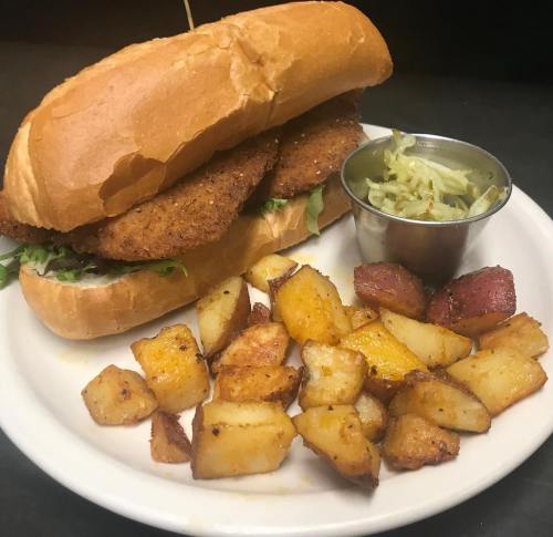 A crispy sandwich with two breaded fillets, served with seasoned potatoes and a small cup of coleslaw.