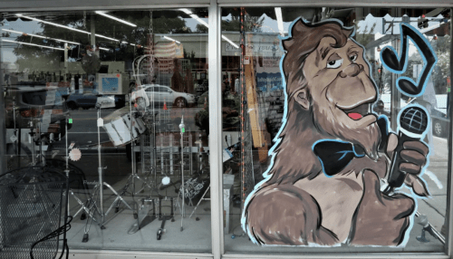 A storefront window featuring a large cartoon gorilla with a microphone and musical notes, surrounded by musical instruments.
