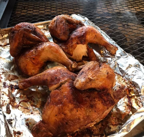 Grilled chicken pieces on a foil-lined tray, with a smoky background and a golden-brown, crispy exterior.