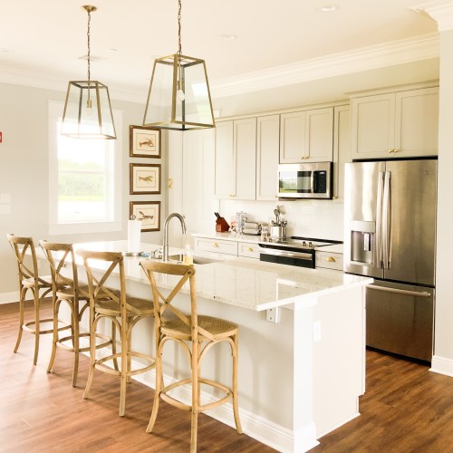 Modern kitchen with light gray cabinets, stainless steel appliances, a large island, and wooden bar stools.