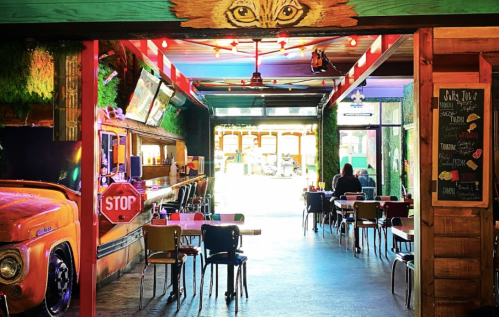 Colorful interior of a restaurant with a bar, tables, and a mural of a fox above. Bright lights and a welcoming atmosphere.