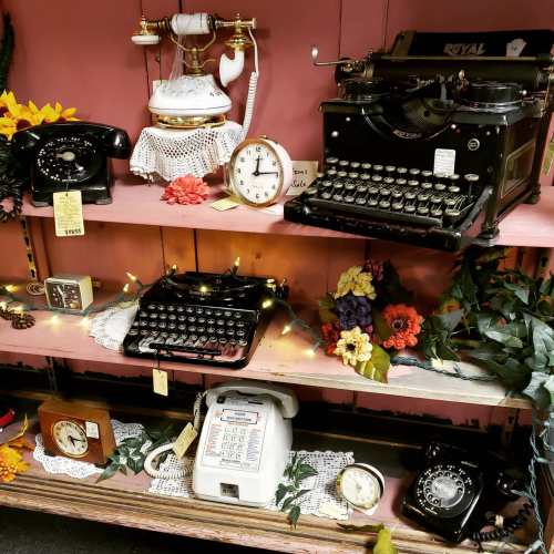 A vintage display featuring old phones, typewriters, and clocks, adorned with flowers and decorative lights.