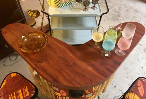 A wooden bar with a curved top, featuring colorful drinks in glasses and an amber ashtray on the surface.