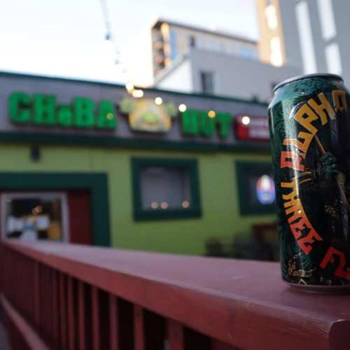 A can of Alpha beer sits on a railing in front of a colorful restaurant with a green exterior.