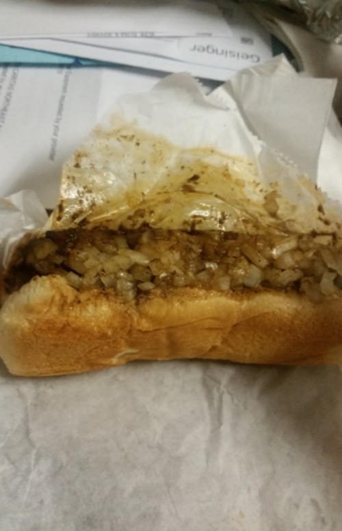 A partially unwrapped sandwich filled with chopped onions and a savory mixture, resting on a piece of paper.