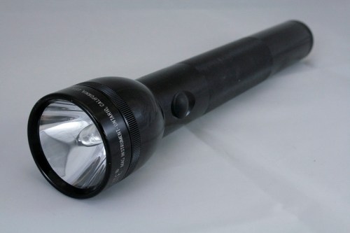 A black flashlight with a shiny reflector and a textured grip, lying on a light background.