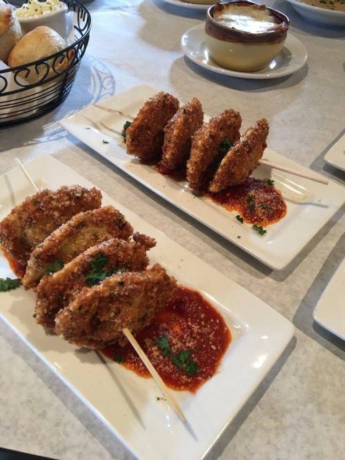 Crispy fried dumplings on skewers served with a red sauce and garnished with cilantro on white plates.