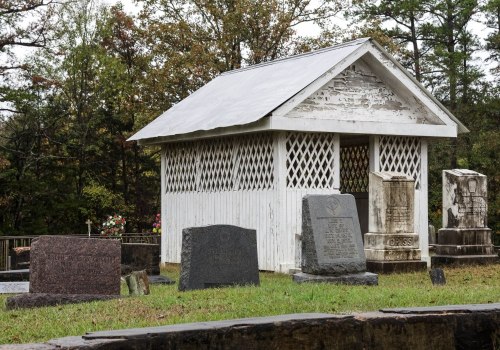 A small white mausoleum surrounded by gravestones in a cemetery, with trees in the background.