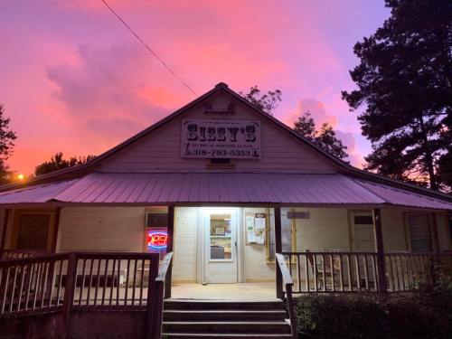 A charming restaurant named "Sissy's" with a glowing "Open" sign, set against a vibrant sunset sky.