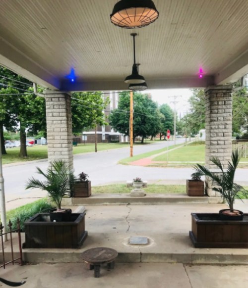 A porch with two hanging lights, potted plants, and a view of a street lined with trees and buildings.