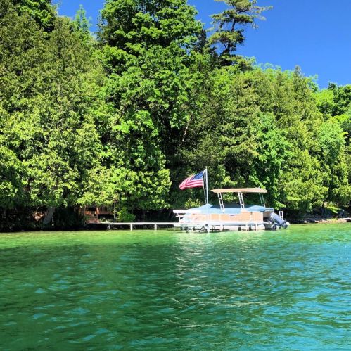 A boat docked by a lush green shoreline, featuring a waving American flag against a clear blue sky.