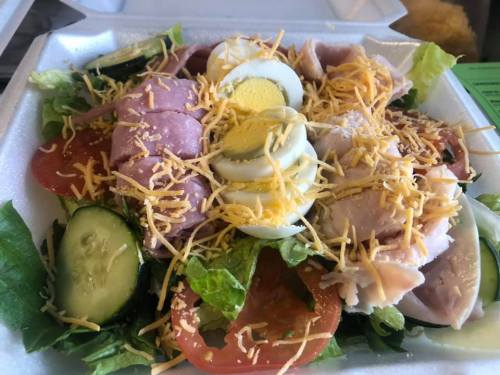 A colorful salad with lettuce, tomatoes, cucumbers, sliced meats, hard-boiled eggs, and shredded cheese.