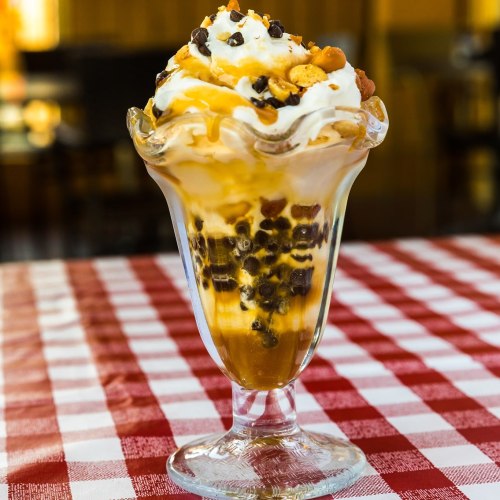 A delicious sundae in a glass, topped with whipped cream, nuts, chocolate chips, and caramel sauce.