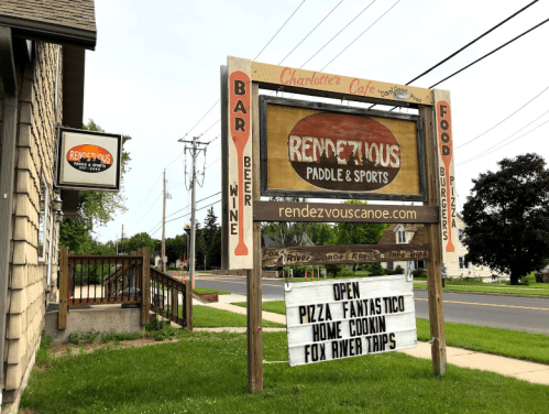 Sign for "Rendezvous Paddle & Sports" featuring food, drinks, and outdoor activities, with a nearby café entrance.