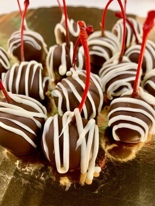 Chocolate-covered cherries with white chocolate drizzle and red stems on a gold background.