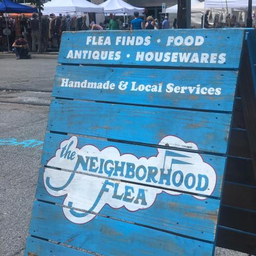 A blue sign for "The Neighborhood Flea" advertising flea finds, food, antiques, housewares, and local services.