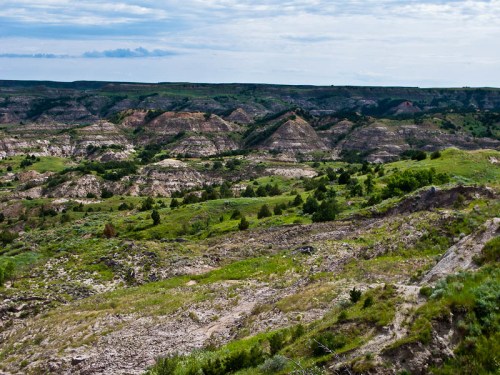 A panoramic view of rolling hills and rugged terrain under a cloudy sky, showcasing lush greenery and rocky formations.